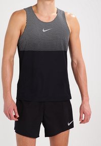 Débardeur sportif noir avec un motif à pois sur la partie supérieure et une section inférieure noire unie, arborant un petit logo Nike argenté.