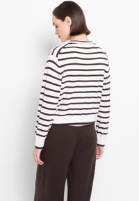 Maglione a righe in bianco e marrone, con orlo e polsini a coste, dal design corto. Indossato con pantaloni marroni scuri.