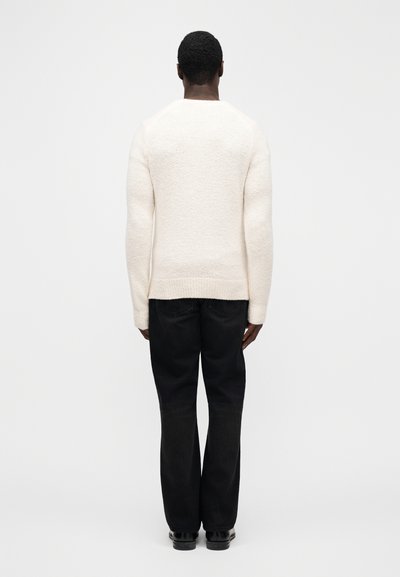 Cream-colored knit sweater with textured finish, round neckline, and ribbed cuffs, paired with dark wash straight-leg jeans and black shoes.