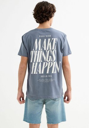 Camiseta de algodón gris con un gran gráfico tipográfico blanco en la parte posterior que incluye un texto motivacional. Manga corta y corte relajado.