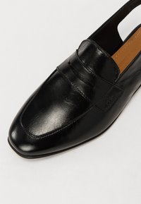 Must have nahkkinga ruudu nina, libisev disain ja dekoratiivne esiõlg. Sile tekstuur ja nähtavad õmblusaktsendid.