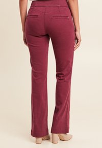 Bordeaux gekleurde slim fit broek met een gladde textuur, voorzien van platte zakken op de achterkant en een uitlopende pijpdesign. De zoom heeft een nette afwerking.