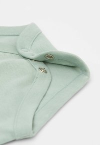 Miętowa bawełniana tkanina z żeberkowym kołnierzykiem, zatrzaskami i zaokrąglonymi brzegami. Miękka tekstura z gładkim detalem przeszycia.