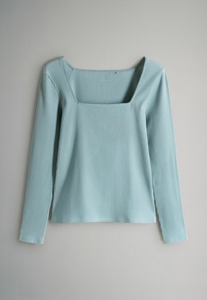 Svetlomodrý rebrovaný top s dlhým rukávom a štvorcovým výstrihom položený na šedom povrchu.