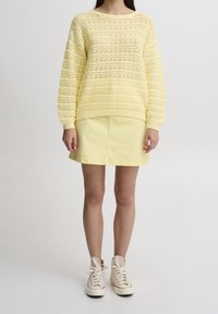 Suéter amarillo de punto con un patrón texturizado a rayas, combinado con una falda amarilla a juego y zapatillas altas beige.