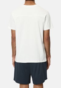 Weißes T-Shirt mit kurzen Ärmeln und Rundhalsausschnitt, aus Baumwolle, von hinten betrachtet, kombiniert mit dunkelblauen Shorts.