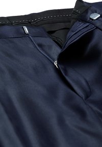 Marineblauer Stoff mit glatter Textur, ausgestattet mit einem Reißverschluss und metallischen Beschlägen am Taillenbund. Innentaschendetail sichtbar.