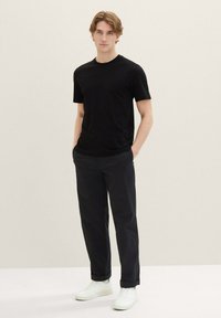 Svart t-skjorte med korte ermer og rund hals, kombinert med mørke bukser og hvite joggesko. Stoffet virker glatt og lett.