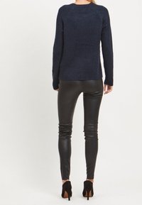 Pull côtelé bleu marine avec un col rond, des manches longues et une coupe décontractée, associé à un pantalon en cuir noir ajusté et des chaussures noires à talons hauts.