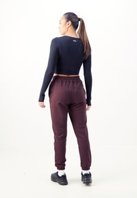 Schwarzes langärmliges Crop-Top und bordeauxfarbene Jogginghosen mit elastischen Bündchen, ausgestattet mit einer Gesäßtasche und kontrastierenden schwarzen Sneakers mit weißen Socken.