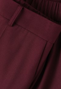 Pantalones de tela burdeos con una textura suave, con una cinturilla plana y pliegues, diseñados para un ajuste estructurado.