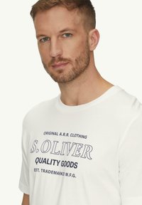 Witte katoenen shirt met een ronde halslijn en korte mouwen, met marineblauwe bedrukte tekst "S. OLIVER QUALITY GOODS." Eenvoudig en casual ontwerp.
