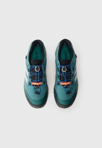 Bottes de randonnée teal et noires avec une tige texturée, des lacets élastiques bleus et des accents réfléchissants. Comprend une étiquette GORE-TEX.