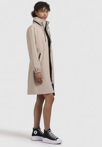 Giacca leggera beige con colletto alto, polsini elasticizzati, zip frontale e due tasche laterali, abbinata a sneakers nere alta.