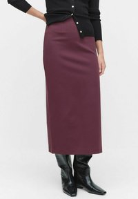 Jupe maxi bordeaux en tissu doux et extensible, avec une coupe droite et une texture lisse, assortie à des bottes noires en cuir crocodile.