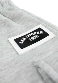 Tissu gris avec une étiquette blanche et noire affichant "LEE COOPER 1908" en texte blanc. Le matériau semble doux avec une surface légèrement texturée.