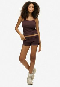 Czerwono-brązowy tank top w paski oraz dopasowane szorty wykonane z miękkiego materiału. Model nosi jasne trampki i skarpetki do kostek. Minimalistyczny design.