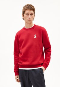 Rode sweatshirt van een zachte katoenmix. Kenmerken zijn een wit lintlogo op de borst en een gebreide kraag, manchetten en zoom. Gestyled met donkere broek.