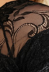 Il tessuto in pizzo nero presenta intricati motivi floreali, con un design a rete testurizzata e un bordo a scallop, evidenziando l'artigianalità delicata.