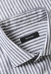 Col de chemise pour homme à rayures verticales bleues et blanches avec une étiquette noire portant le nom "Matinique" à l'intérieur.