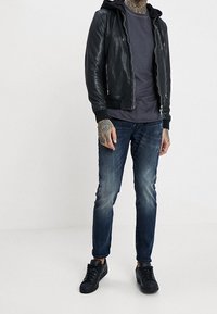Chaqueta bomber de cuero negro con capucha, camiseta gris, jeans de mezclilla azul desgastados y zapatillas negras. Ajuste casual con puños acanalados.