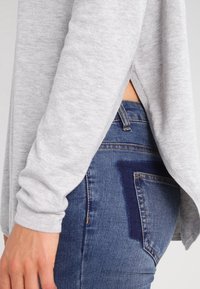 Szary wełniany sweter z bocznymi rozcięciami, w zestawieniu z niebieskimi dżinsami z wybielonymi miejscami. Zbliżenie na fakturę materiału i szwy.