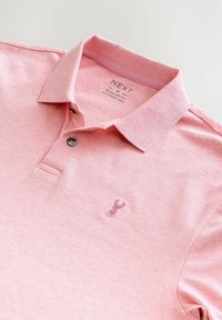 Polo de color rosa claro confeccionado en un tejido texturizado, con un cuello abotonado y un pequeño logo de langosta bordado en el pecho.