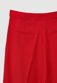Pantalons sur mesure rouges avec une texture lisse, deux poches arrière et une coupe droite avec une ceinture épurée.