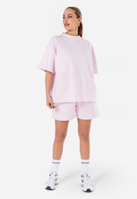 T-shirt en coton rose à manches courtes oversized, associé à un short rose assorti. Porté avec des sneakers blanches et des chaussettes mi-mollet.