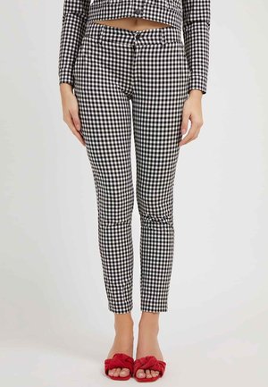 Kvinde iført sort-hvide gingham-bukser og matchende kort skjorte, kombineret med røde åbne slip-on sko mod en ensfarvet baggrund.