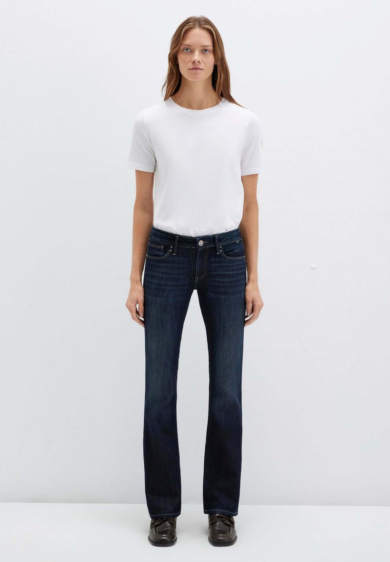 T-shirt bianco a maniche corte abbinato a jeans svasati blu scuro, con design classico a cinque tasche e chiusura con bottone. Tessuto dalla texture liscia.