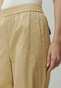 Beige, lichte broek met elastische tailleband en zijzak. Gladde textuur, losse pasvorm, gedetailleerde stiksels en een minimalistisch ontwerp.