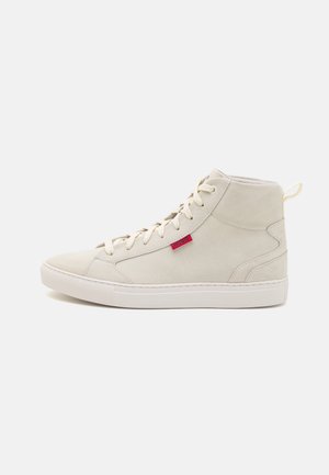 High-top sneakers in beige suede, featuring white rubber sole, round toe, and a red side tag. Smooth texture with lace-up closure.