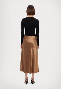 Svart ribbestrikket langermet topp kombinert med et blankt bronsefarget satin midi-skjørt. Modellen har på seg svarte høye hælsandaler. Minimalistisk og elegant design.
