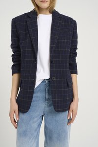Námořnický modrý károvaný blazer s šedým a modrým vzorem, na dva knoflíky a s jednou náprsní kapsou, nošený přes bílý tričko a světlé džíny.