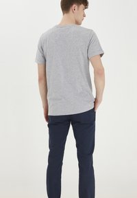 T-shirt grigio a maniche corte con collo rotondo, abbinato a pantaloni blu navy. Il tessuto sembra morbido e informale, con una vestibilità comoda.