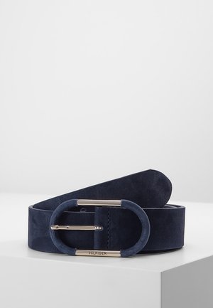 Marineblauer Veloursledergürtel mit ovaler Schnalle, die silberne Metallakzente zeigt, und mit „Hilfiger“ auf dem unteren Teil der Schnalle graviert.