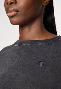 Black, slightly distressed sweatshirt with a round neckline, featuring a textured Champion logo embroidered on the chest.