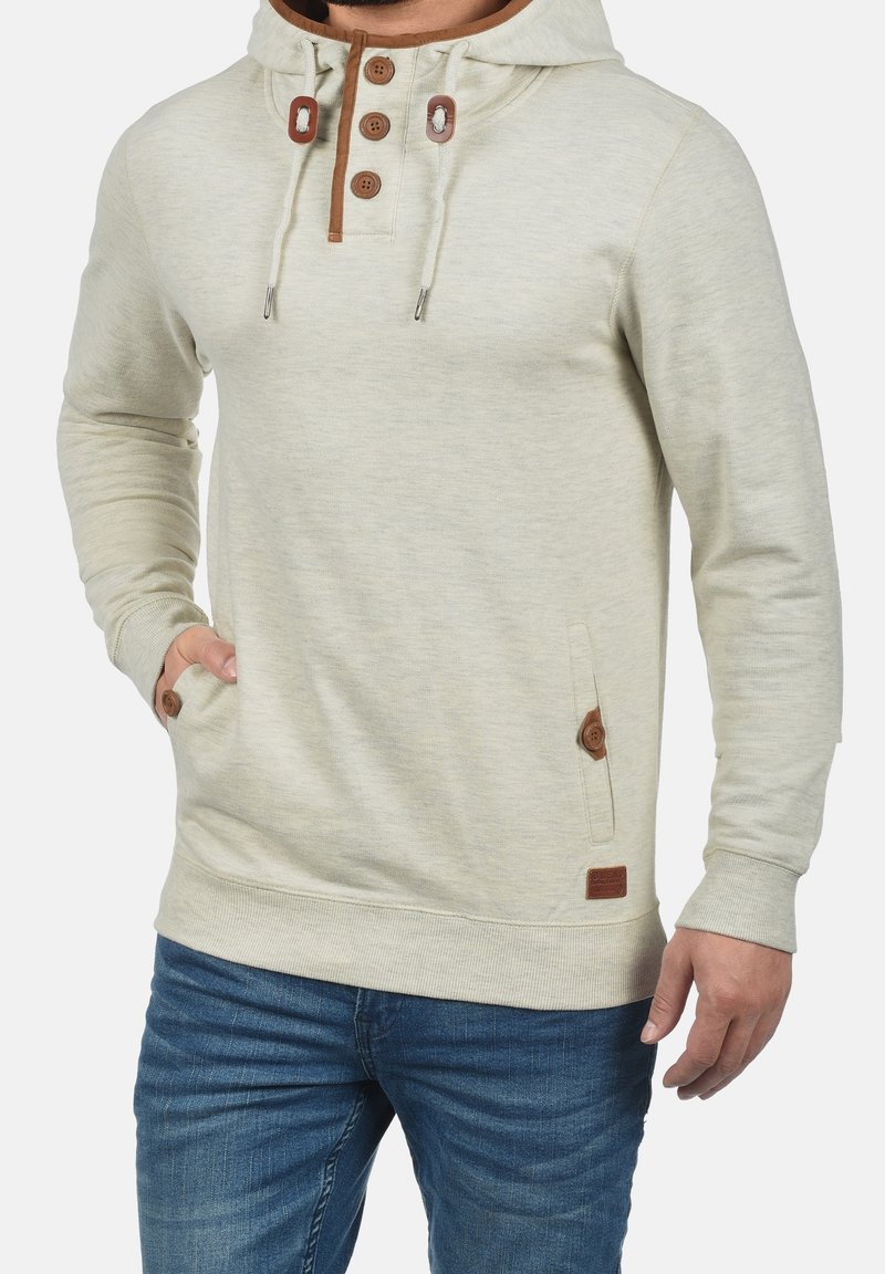 Felpa leggera color beige con cordino beige, patta con tre bottoni, tasche laterali con dettagli marroni e polsini e orlo a coste.