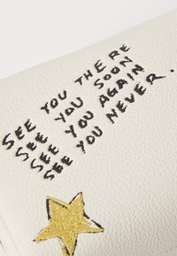 Pochette en cuir blanc avec du texte manuscrit noir : "À TOUT À L'HEURE, À NOUVEAU, JAMAIS VU," et un détail étoile brodé en or.