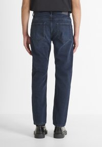 Jeans de mezclilla azul oscuro con un diseño de pierna recta, bolsillos traseros visibles y un dobladillo limpio. Llevados con botas negras, vistos desde atrás.