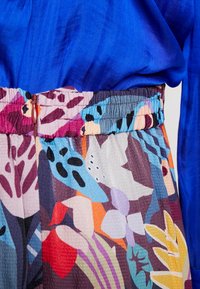 Kolorowa, wzorzysta tkanina z motywami kwiatowymi i liściastymi, posiadająca marszczony pas. Towarzyszy jej intensywnie niebieska góra o gładkiej fakturze.