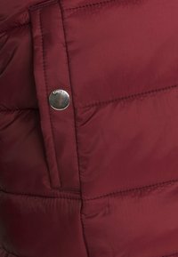 Burgundowa kurtka puchowa o gładkiej, błyszczącej fakturze. Posiada boczną kieszeń i srebrny guzik z grawerunkiem "ONLY".