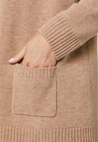 Beige gebreide cardigan met ribbelmanchetten en zak, voorzien van een zachte textuur en een relaxte pasvorm.