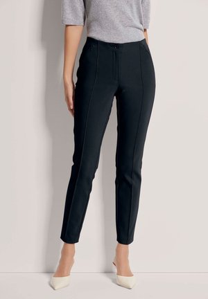 Zwarte slim-fit broeken met een gladde textuur, voorzien van voorzakken en subtiele stikdetails, gecombineerd met beige hoge hakken.