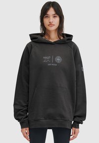 Czarna bluza z kapturem, kieszenią kangurzą i ściągaczami. Na przodzie znajduje się napis "HALO" i "OFF PITCH" w kontrastującym białym kolorze.