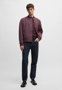 Maroon bomber jacket with ribbed cuffs, paired with dark blue jeans and black lace-up shoes. Smooth texture, fitted design. No visible patterns.