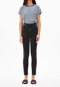 Camiseta de manga corta a rayas en azul y blanco, jeans ajustados negros de tiro alto y sandalias negras de pala con suela plana.