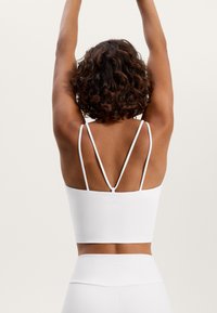 White athletic crop top with thin, adjustable straps, featuring a seamless design and a subtle brand logo on the back.