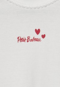 Weißes Baumwoll-T-Shirt mit rotem Drucktext "Petit Bateau" und zwei kleinen Herzen darüber; Detail mit gewelltem Halsausschnitt.
